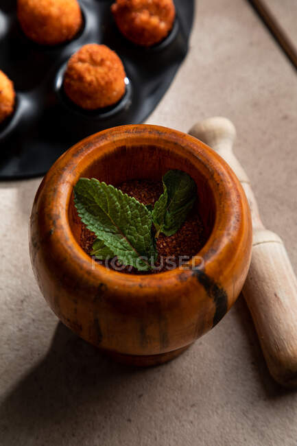 From above of wooden mortar with pepper powder and mint leaves near pestle placed near deep fried cheese balls — Stock Photo
