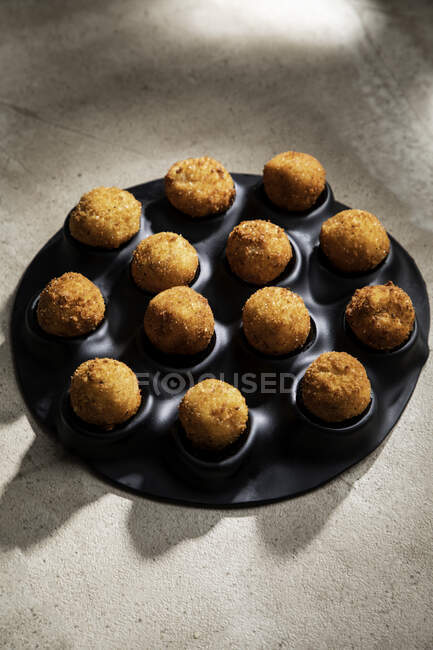 Alto ángulo de sabrosas bolas de queso tostado en bandeja para hornear sobre mesa de hormigón en la cocina - foto de stock
