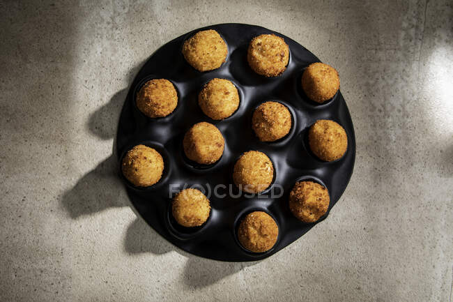 Alto ángulo de sabrosas bolas de queso tostado en bandeja para hornear sobre mesa de hormigón en la cocina - foto de stock