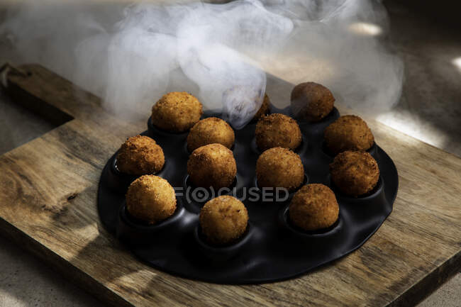 High angle of tasty roasted cheese balls in baking dish on wooden cutting board in kitchen in ice steam — Stock Photo