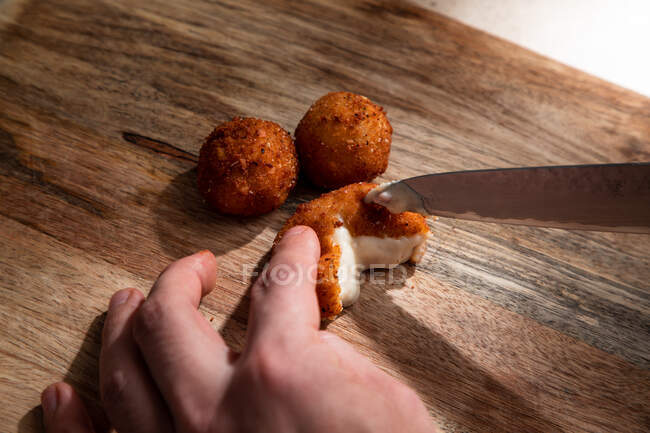 From above of crop anonymous cook cutting crispy deep fried cheese ball on wooden cutting board — Stock Photo
