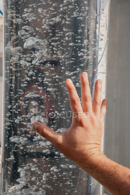 Crop anonymous person with hand placed on glass transparent surface with baubles in water — Stock Photo