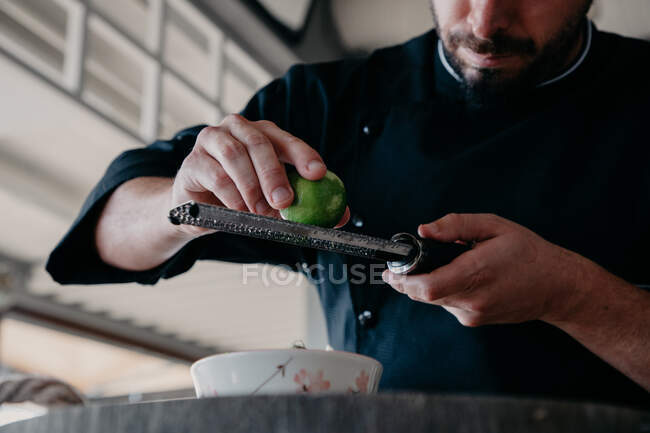 Ritagliato uomo concentrato irriconoscibile sfregamento scorza di frutta al lime durante il processo di cottura al bancone della cucina elegante — Foto stock