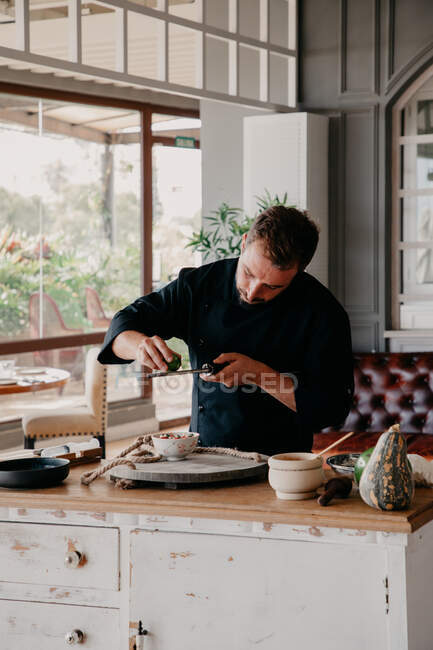 Homme concentré frottant zeste de fruits pendant le processus de cuisson au comptoir de la cuisine élégante — Photo de stock