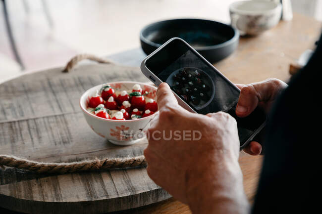 Сверху сзади вид неузнаваемого шеф-повара в форме, фотографирующего на мобильный телефон еду в миске в ресторане — стоковое фото