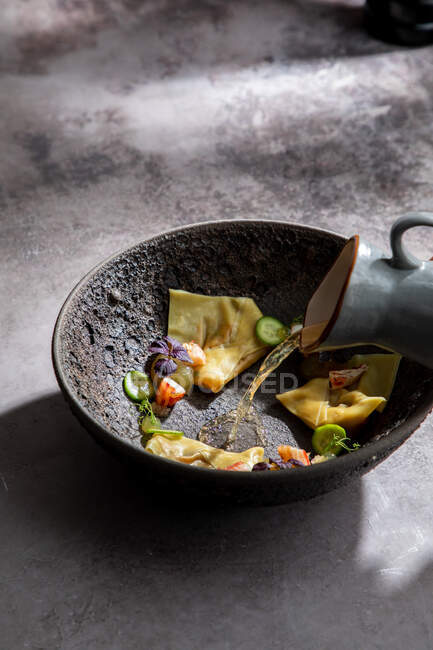Recadrer un cuisinier anonyme en ajoutant du bouillon dans un bol avec des boulettes japonaises traditionnelles tout en préparant le repas au restaurant — Photo de stock