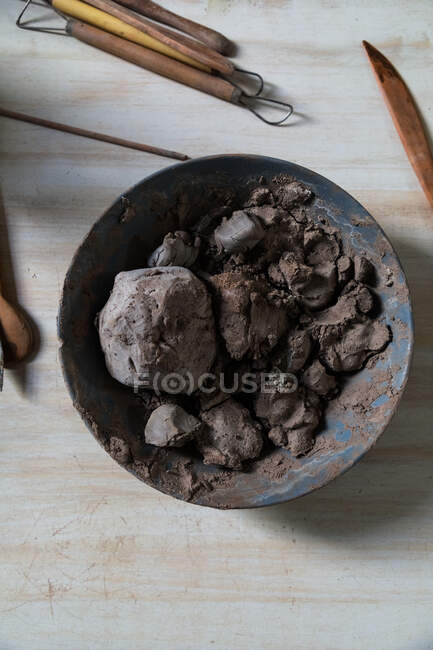 Top view of bowl with soft clay placed on wooden table near set of potter tools in workshop — Stock Photo