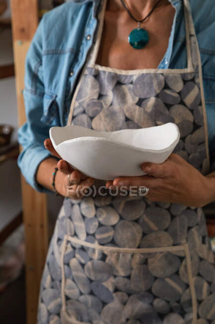 Crop unrecognizable artisan in apron demonstrating creative ceramic plate in workshop — Stock Photo