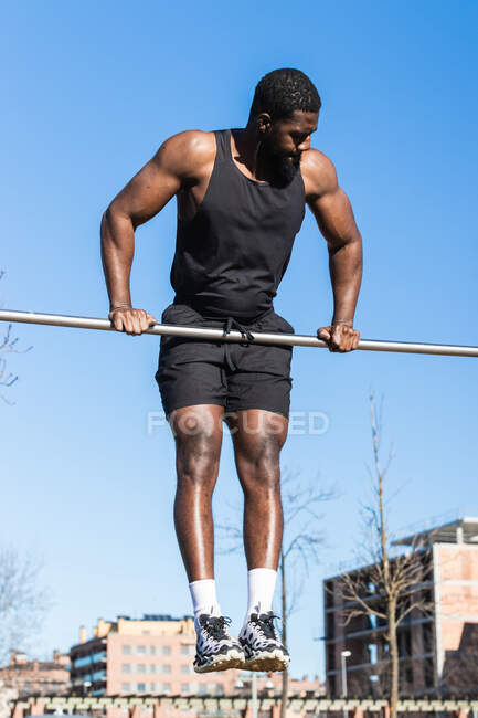Красивый мускулистый афроамериканец-спортсмен во время тренировок в городе подтягивается на металлическом столбе — стоковое фото