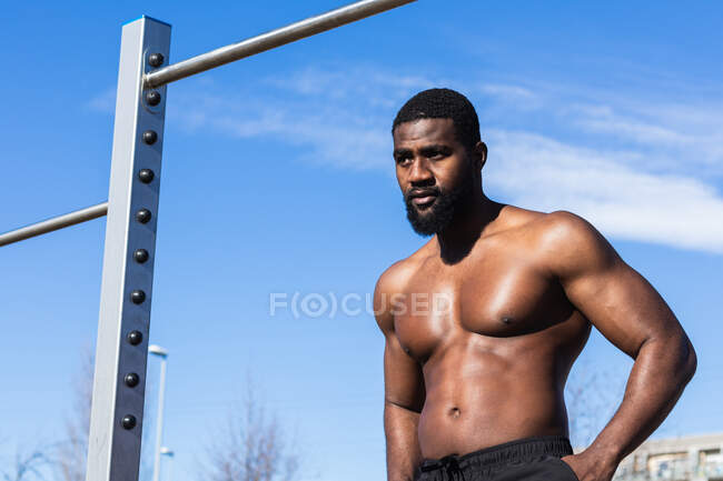 Безсоромний чорний чоловічий спортсмен, який стоїть на стегнах, відпочиваючи під час тренувань на сонці. — стокове фото