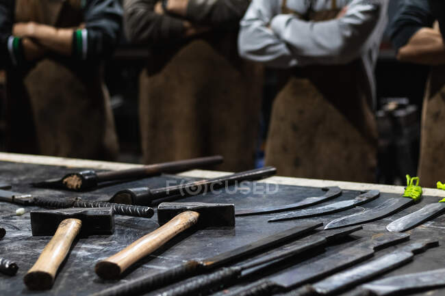 Reihen von verschiedenen Metallinstrumenten, die in einer Schmiede mit unkenntlichen Arbeitern auf dem Tisch stehen — Stockfoto