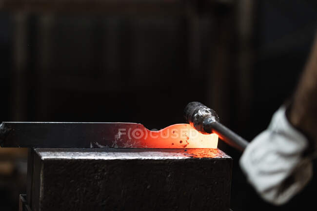 Unbekannter Handwerker hämmert bei Schmiedeprozess in Werkstatt heißes Eisenteil auf Amboss — Stockfoto
