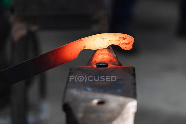 Crop anonymous craftsmen in gloves making hot metal detail with hammer in blacksmith workshop — Stock Photo