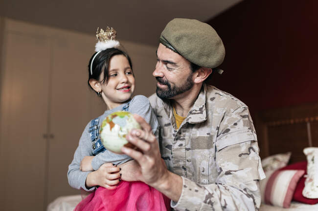 Снизу позитивный солдат разговаривает с дочерью и указывает на место на земном шаре, прежде чем идти служить в армию — стоковое фото