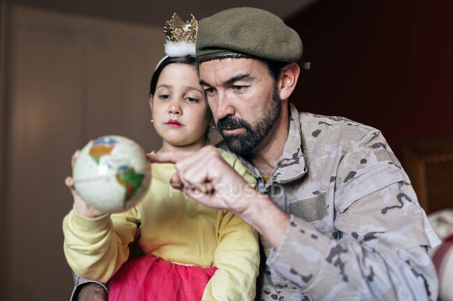 Low angle of soldier talking to daughter and pointing at place at globe before going to serve in army — Stock Photo
