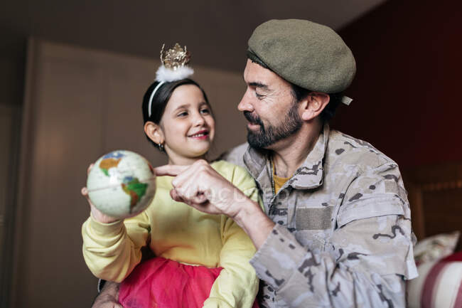 From below of positive soldier talking to daughter and pointing at place at globe before going to serve in army — Stock Photo