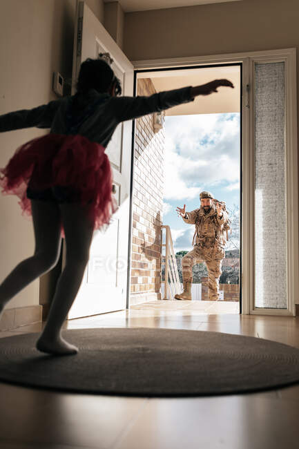 Low angle of surprised daughter running towards father returning from military service standing in doorway — Stock Photo