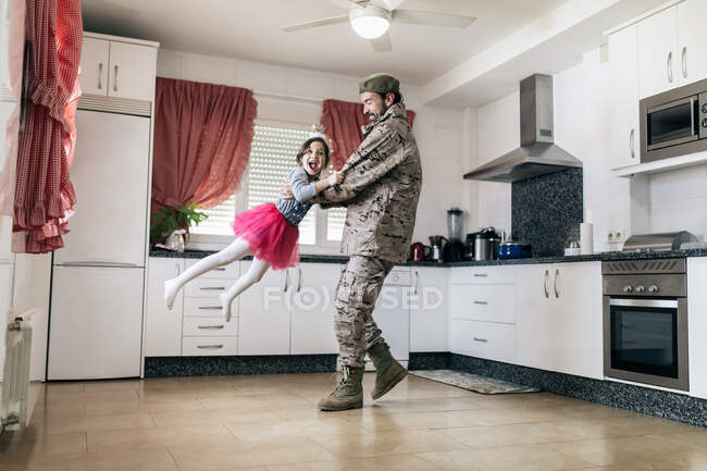 Linda hija jugando a su padre en uniforme militar en la cocina - foto de stock