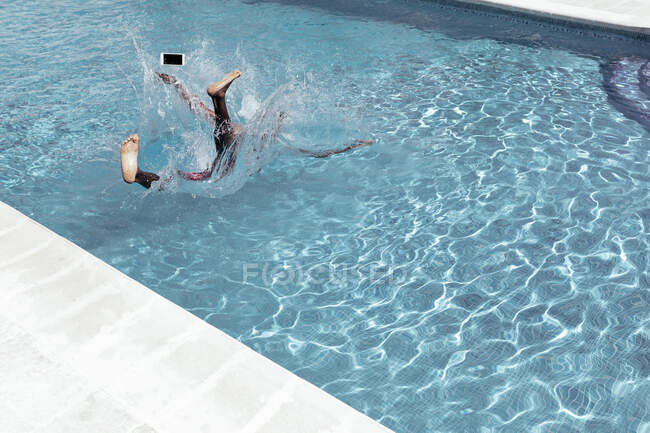 Hombre afroamericano anónimo cayendo en la piscina con teléfono inteligente y salpicaduras de agua - foto de stock