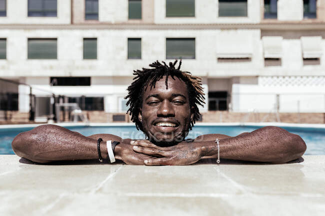 Entzückter afroamerikanischer Mann lehnt am Pool, genießt den Sommerurlaub und blickt in die Kamera — Stockfoto