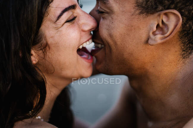African American male traveler kissing sincere female partner standing against ocean during summer trip — Stock Photo