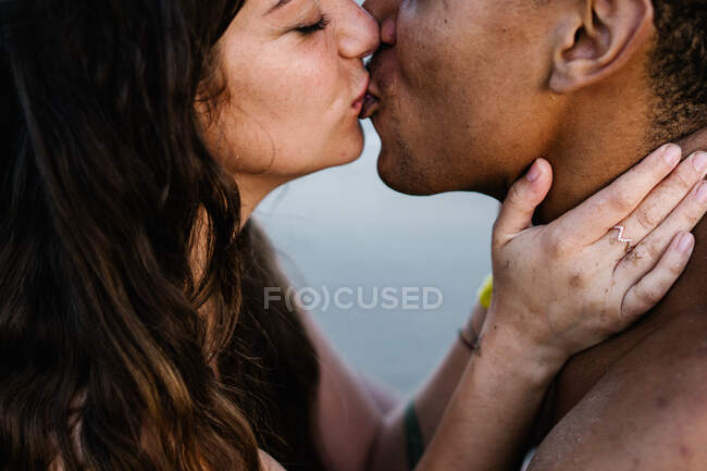 Anonymous African American male traveler kissing sincere female partner standing against ocean during summer trip — Stock Photo