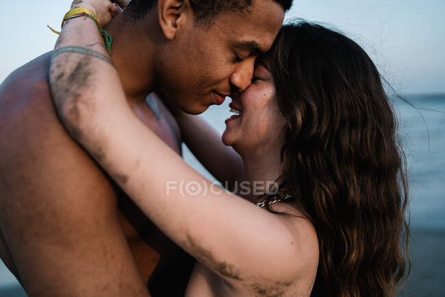 Афроамериканець цілує щирого партнера, який стоїть проти океану під час літньої подорожі. — стокове фото