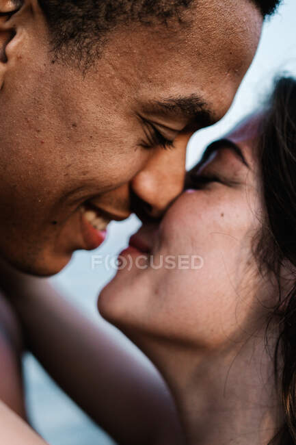Afrikanischer Reisender küsst aufrichtige Partnerin, die während Sommerreise gegen Ozean steht — Stockfoto