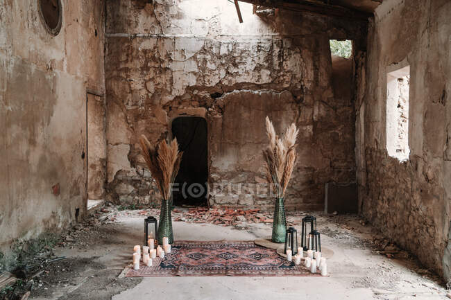 Aged building with fluffy dry plants in vases near burning candles and lanterns on ornamental carpet — Stock Photo