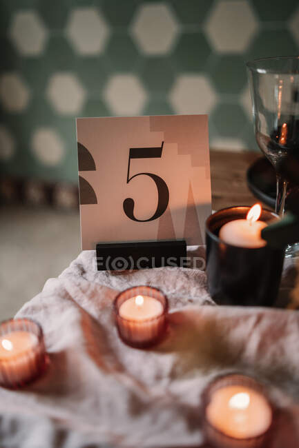 Decoration with number and similar flaming candles near wine glass on crumpled fabric during festive event — Stock Photo