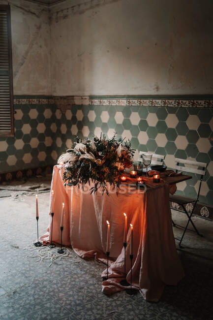 Blühende Blumen auf Tischdecke mit Zahl und brennende Kerzen an Zierwand bei Festveranstaltung in Cafeteria — Stockfoto