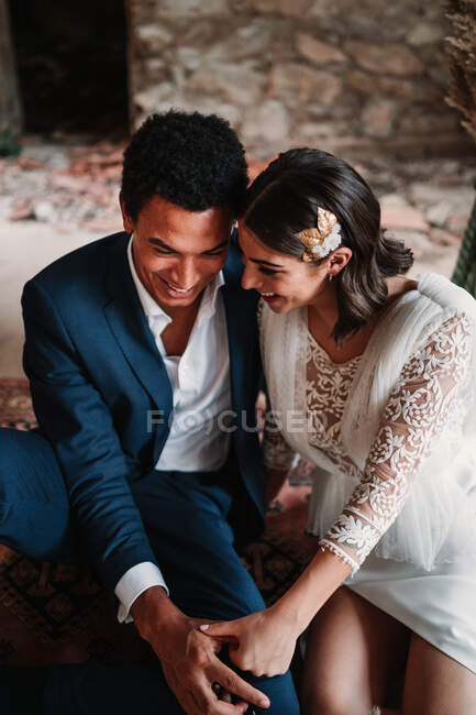 Von oben sitzt ein junges, fröhliches Brautpaar in schicken Hochzeitskleidern auf dem Boden im Grunge-verlassenen Bauzimmer — Stockfoto