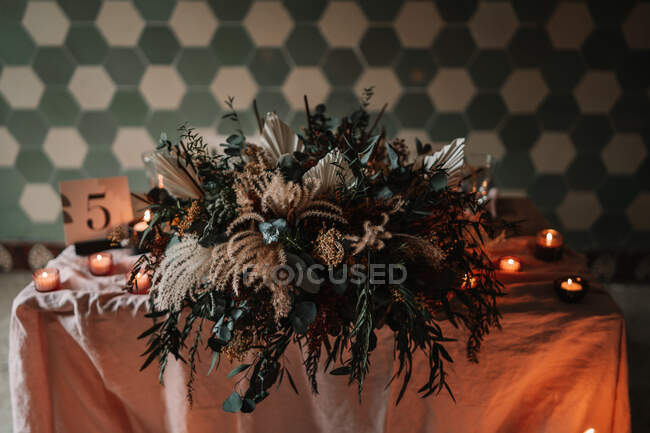 Flores florecientes sobre mantel con número y velas encendidas contra pared ornamental durante evento festivo en cafetería - foto de stock