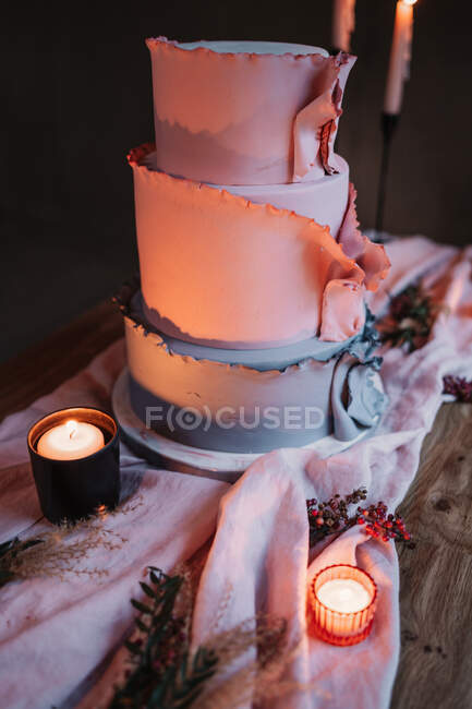 Delicious tiered cake served on wooden table and surrounded by burning candles in dark room — Stock Photo
