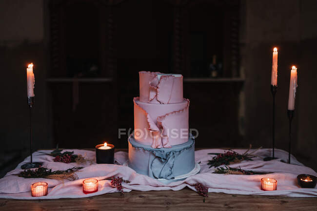 Délicieux gâteau à plusieurs niveaux servi sur une table en bois et entouré de bougies allumées dans une pièce sombre — Photo de stock