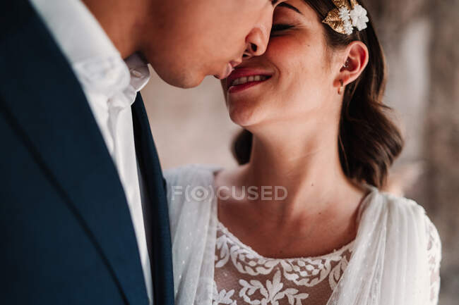 Side view of cropped unrecognizable romantic ethnic newlywed couple in elegant clothes bonding tenderly with eyes closed in light wedding studio — Stock Photo