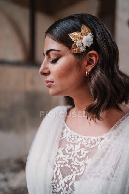 Encantadora jovem noiva étnica em elegante vestido branco de pé com os olhos fechados no estúdio de casamento leve — Fotografia de Stock