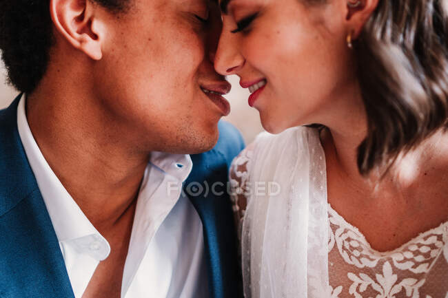 Crop young happy newlywed couple wearing posh wedding clothes sitting on floor face to face — Stock Photo
