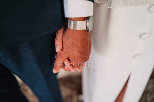 Зверху безликі новоспечені пари носять елегантний одяг, який ніжно тримає руки під час весільної церемонії — стокове фото