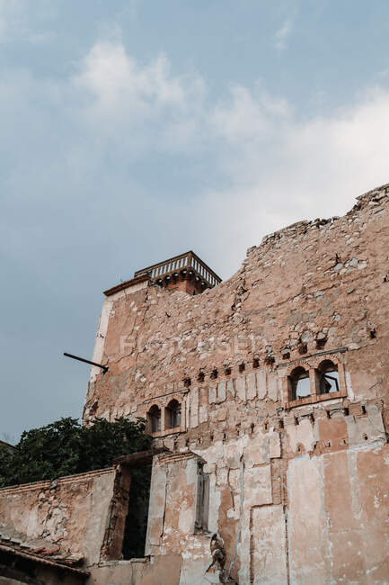 Постаревшая кладка здания снаружи с выветривающимися стенами под облачным небом в дневное время — стоковое фото
