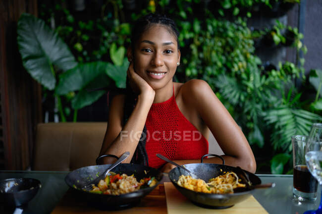 Retrato de mujer latina afro joven atractiva con rastas en un top rojo del ganchillo posando en restaurante asiático, Colombia - foto de stock