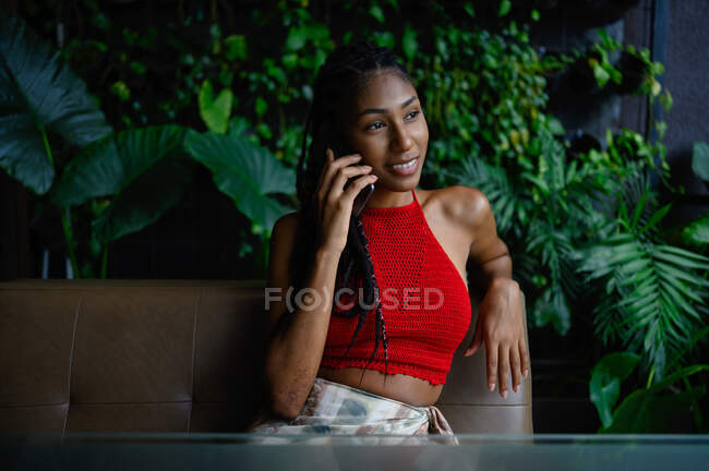 Portrait of happy attractive young afro latin woman with dreadlocks speaking on the phone at restaurant table, Colombia — Stock Photo