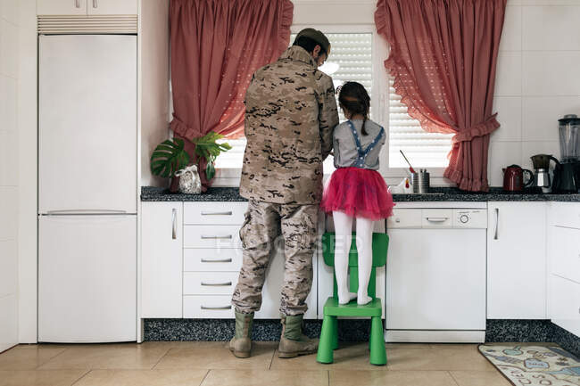 Rückansicht des Militärvaters in Uniform, der mit Kind in der Küche steht und gemeinsam Geschirr spült — Stockfoto