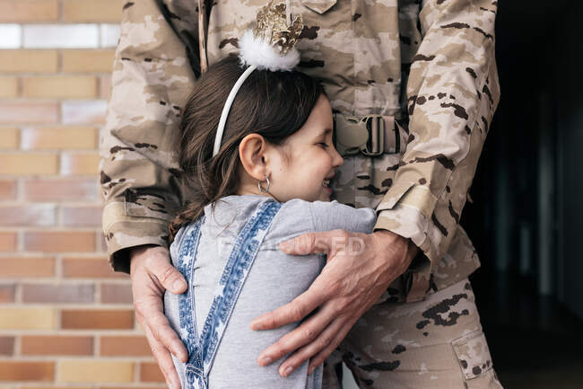Cute daughter tenderly embracing father in military uniform at doorstep after arrival — Stock Photo