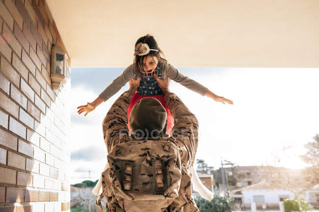 Vue de face de l'homme militaire lançant une petite fille debout à la porte de la maison après le retour au pays — Photo de stock