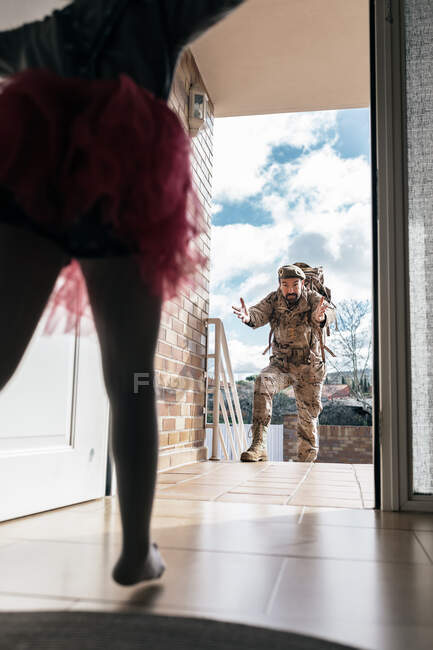 Baixo ângulo de filha surpreendida correndo em direção ao pai retornando do serviço militar em pé na porta — Fotografia de Stock