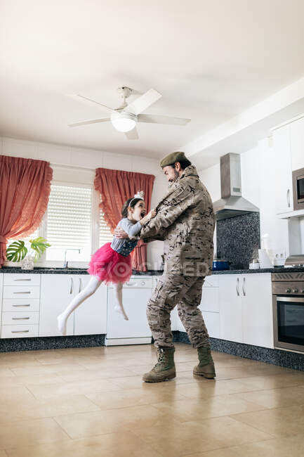 Cute daughter playing her father in military uniform in the kitchen — Stock Photo