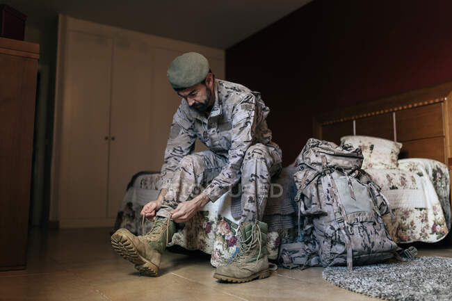 Angle bas du soldat enfilant des bottes pendant qu'il se prépare au service militaire à la maison — Photo de stock