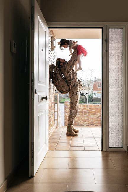 Вид збоку військового, який кидає маленьку дівчинку, стоячи біля дверей будинку після повернення додому — стокове фото