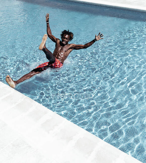 Astonished African American male in shorts falling into swimming pool — Stock Photo